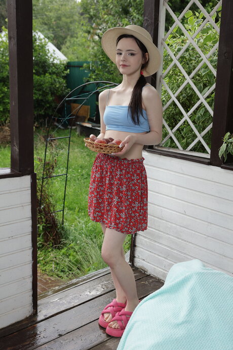Sweet teen Dakota Doll picks up fruit while going nude on a covered porch
