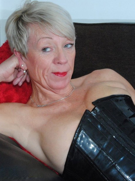 Hot mature Shazzy B in latex & boots displays her big saggy boobs on the couch