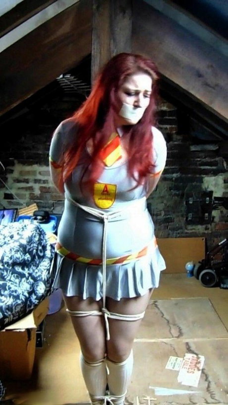 Redheaded plumper Mada Rose is tied to an attic post while clothed and gagged