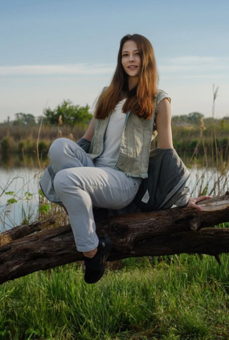 Young redhead Maat makes her nude debut upon a tree next to a body of water