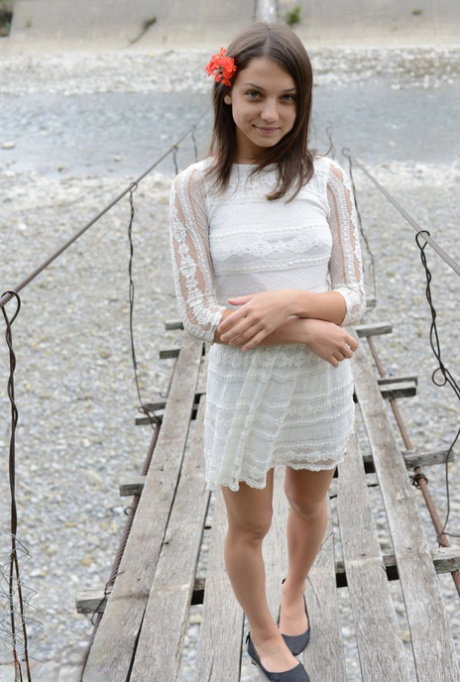 Petite teen wears a flower in her hair while posing nude on suspension bridge