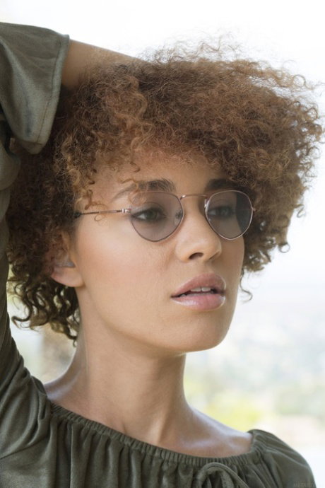 Hot young girl with curly hair removes glasses and a top to get naked in heels