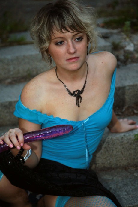 Blonde girl masturbates with a sex toy on the steps of a building