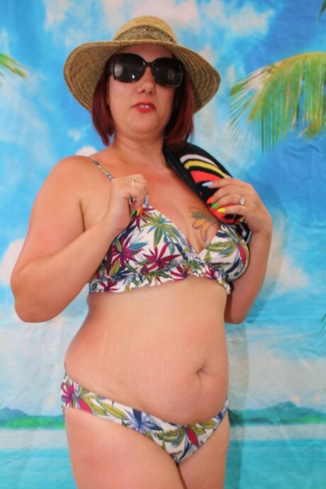 Mature woman Sara Banks takes off her hat and shades while wearing a bikini