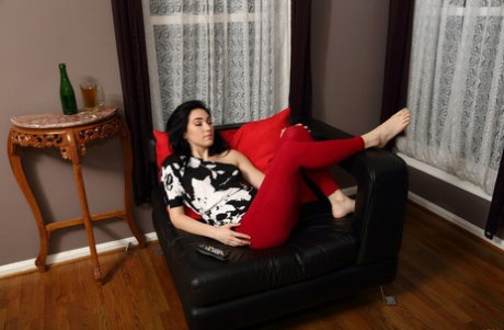 Dark-haired teen Aria Alexander removes red pants before masturbating on a sofa