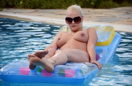 Natural blonde Kelly Fox lays on an air mattress wearing sunglasses only
