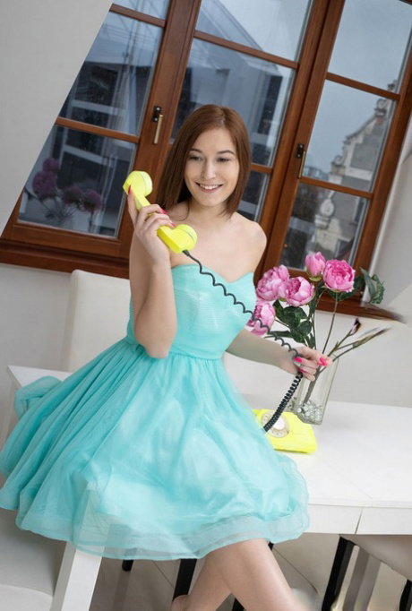 Young redhead removes a pretty dress and underwear to get naked on a table