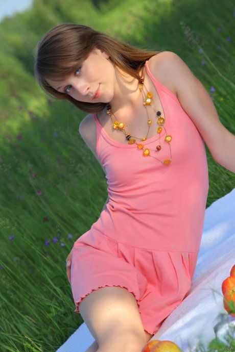 Naked teen holds a tomato while posing on a blanket in a field