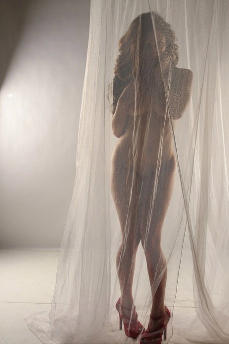 Amateur model Lily Xo poses naked behind sheer curtains in high heels
