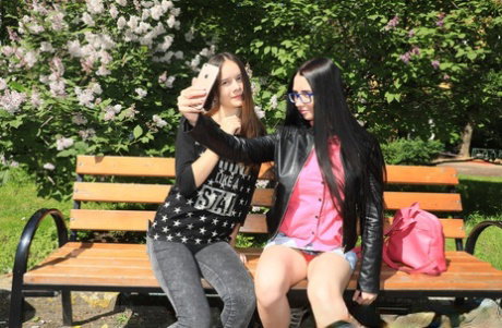 Pretty teens take a selfie on a public bench before having lesbian sex
