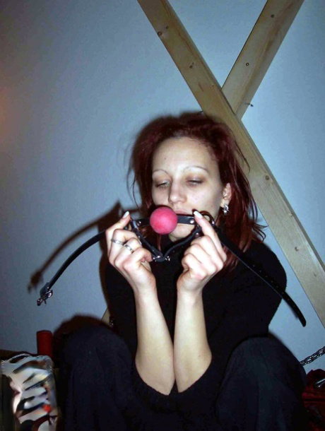 Clothed redhead affixes a ball gag while sitting afore a St Andrew's Cross