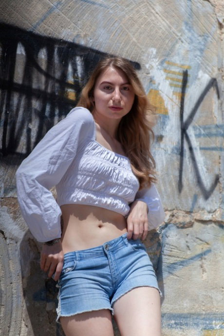 Teen solo girl removes her clothes to pose nude against graffiti covered walls