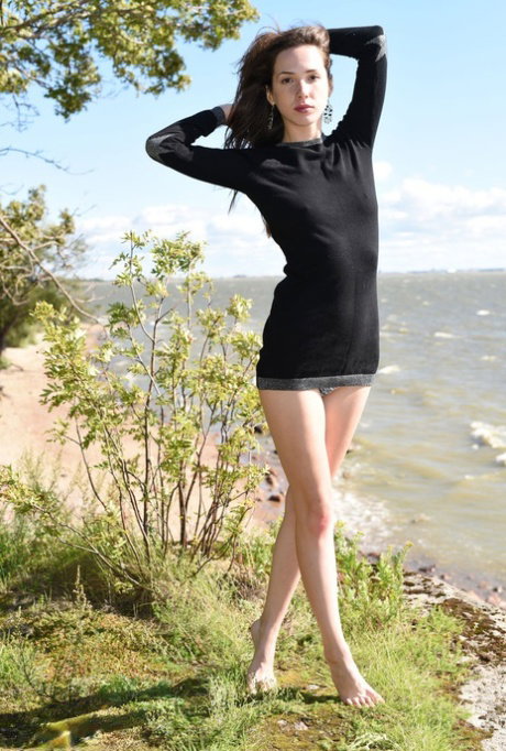 Barefoot teen Dama crosses her bare legs after getting naked by the water