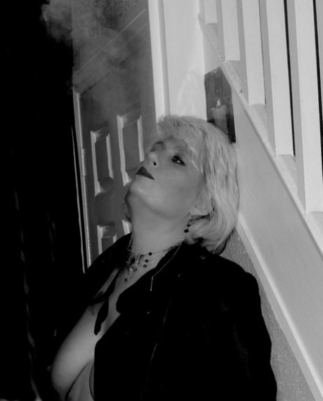 Older blonde lights a cigarette while showing her bare breasts and pussy