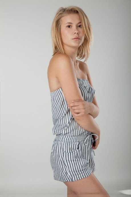 Innocent blonde girl lets her clothes fall away to pose nude on a junk of wood