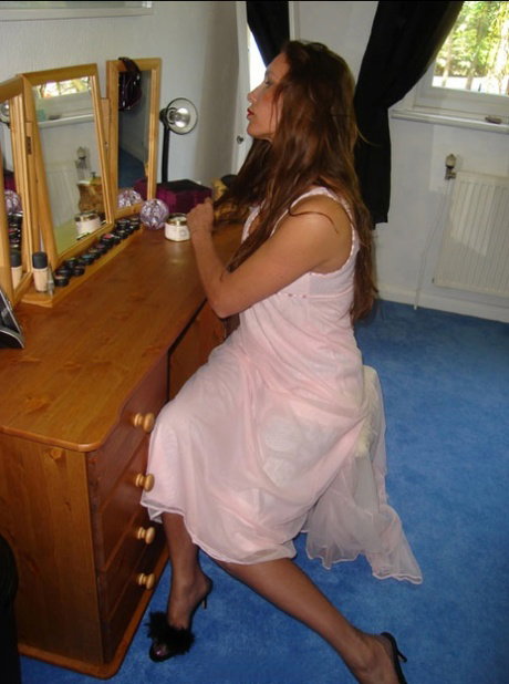 Older woman brushes her long hair in a mirror wearing nylons and garter belt