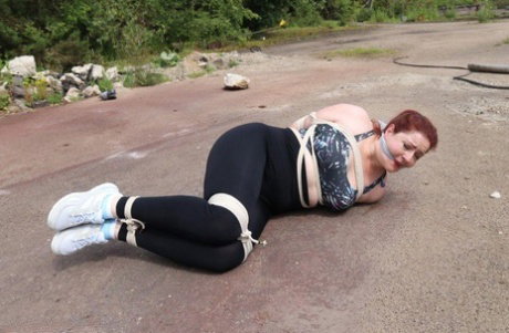 Redheaded girl Mada Rose is left on a paved lot while tied up