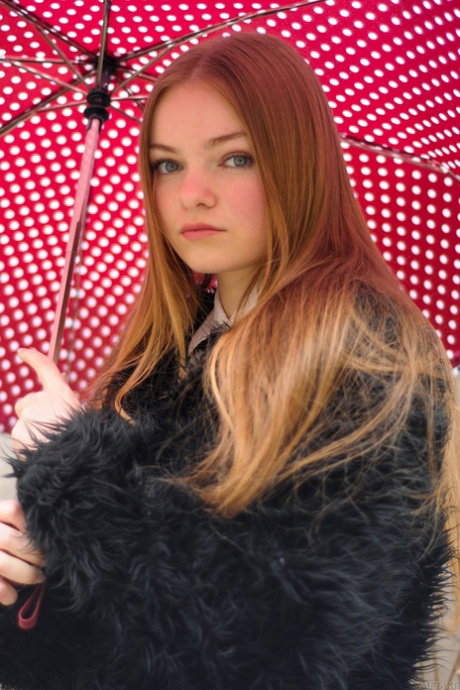 Young redhead Bridgit A takes off a coat and shiny lingerie to pose nude