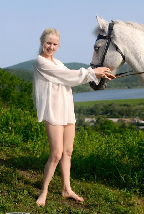 Hot blonde with long hair gets totally naked next to a saddled horse
