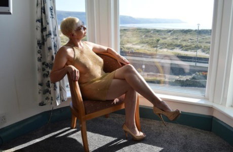 Big titted older woman Barby Slut showcases her bald twat in front of a window