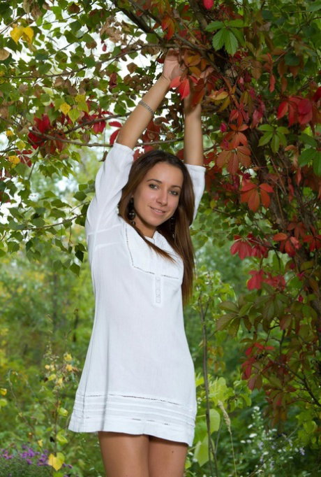 Tall brunette teen strips naked in a garden under an apple tree