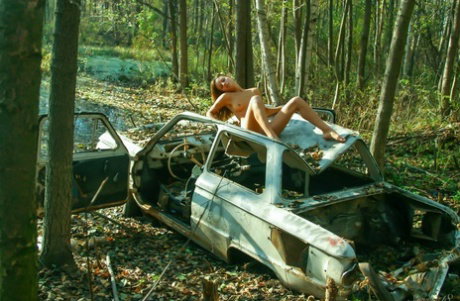 Leggy teen girl poses naked in the woods atop a wrecked vehicle