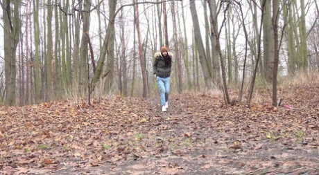 Dark-haired girl squats for a pee on leaf covered ground on a chilly day