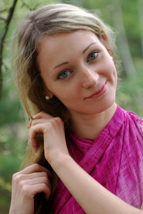 Young blonde Nora A shows her naked boobs under an apple tree near a lake
