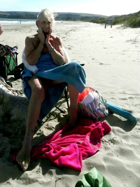 Older blonde Sparkle poses in a bikini while at a sandy beach