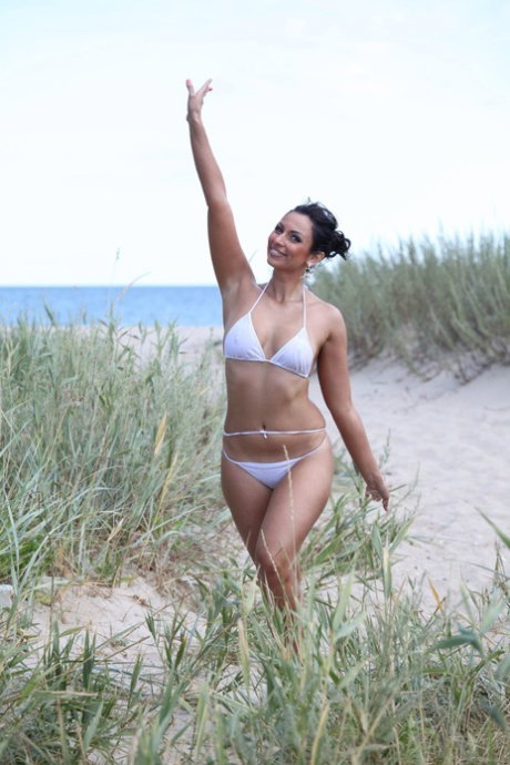 Beautiful brunette gets totally naked on a beach in a playful manner
