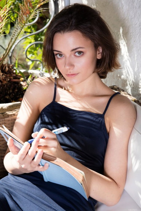 Brunette teen covers her naked body with a notebook on a patio