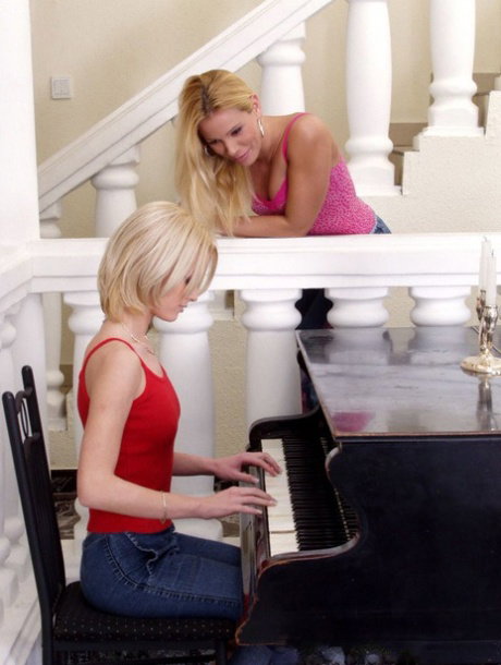 Blonde girls indulge in lesbian play upon a bench while at a grand piano