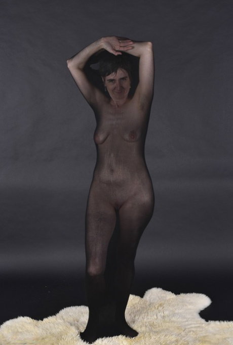 Naked mature woman encases herself in a stocking atop a rug