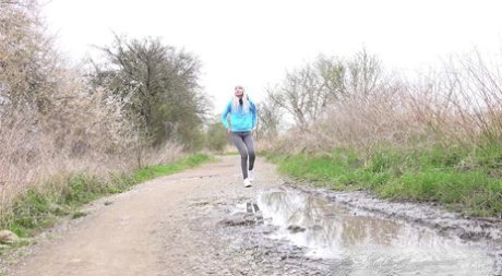 Blonde girl Mistica pees in a puddle on a dirt road through the countryside