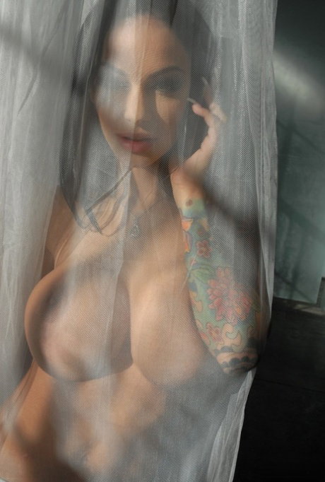 Latina Angelina Valentine talks on the phone as she poses behind the curtain