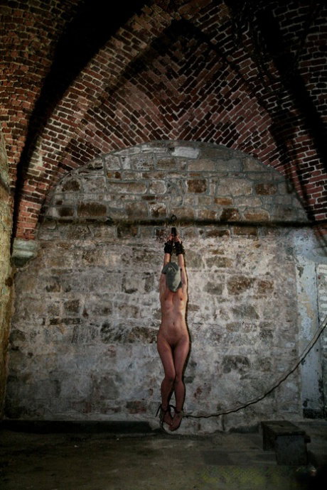 Naked blonde Mirela is whipped by captors while chained to cellar wall
