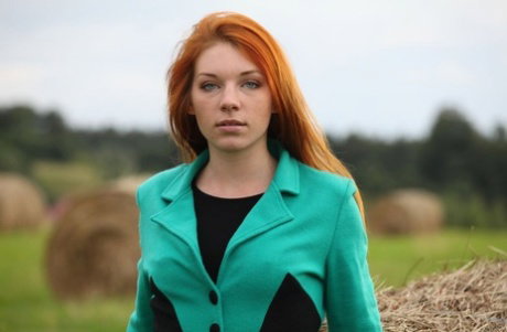 Redheaded teen Amber A gets totally naked against a round bale in a field