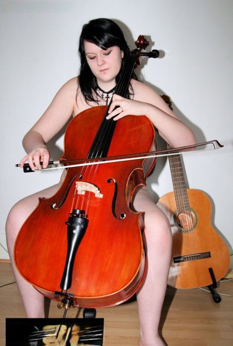 Raven-haired MILF Bhala Sada sitting in a chair playing the cello in the nude