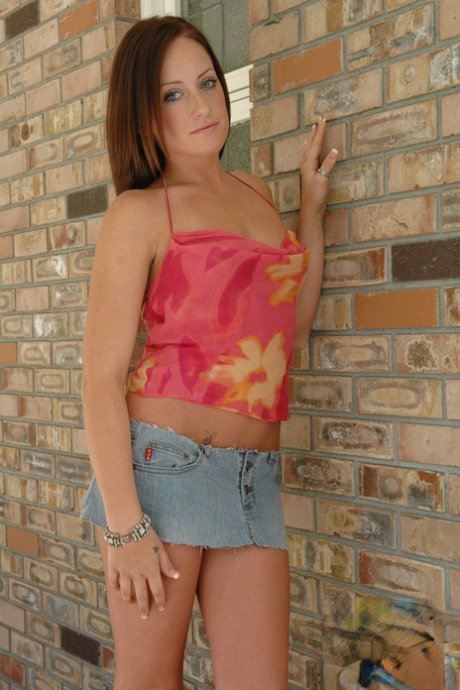 Redhead amateur Kylie places hands over her naked tits against a brick wall