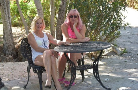Middle-aged lesbians kiss while seated at a patio table in a backyard setting